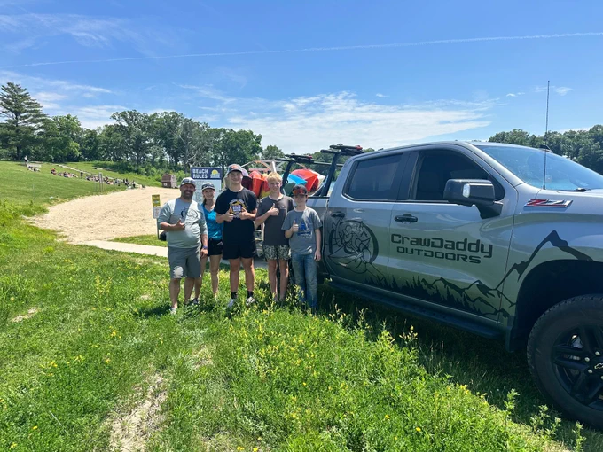 7th grade students standing with the owner of CrawDaddy Outdoors in front of their truck with the kayaks being pulled behind.