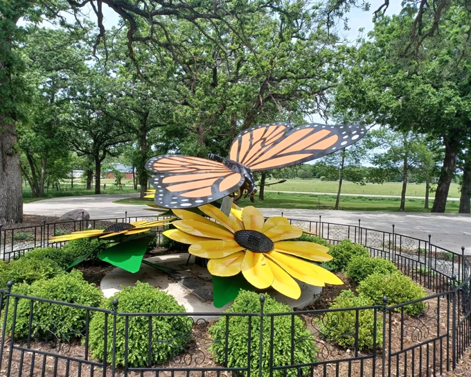 A sculpture of a monarch butterfly hovering over yellow flowers.