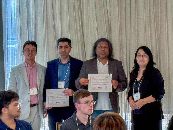 Four people stand together in a hotel conference room before floor-length curtains, wearing conference lanyards. Two hold framed award certificates. Dr. Muhammad Amith, second from right in a gray blazer and white shirt, holds his Best Paper Award certificate at IEEE ICHI 2026 in Minneapolis.

