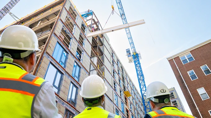Members of the construction team look up as the crane hoists the final beam to the top of Pachyderm Place for its topping off ceremony. Photo: Alonso Nichols/Tufts University