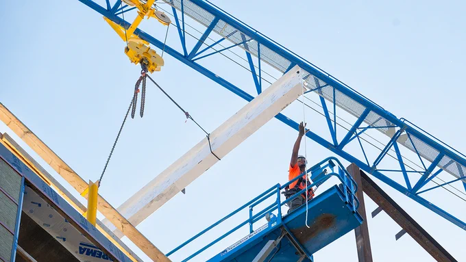 A construction work at the top of Pachyderm Place grabs hold of the final beam during the topping off ceremony. Photo: Alonso Nichols/Tufts University