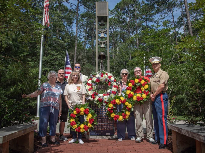 Gold Star family members, veterans, and a Marine pose with ceremonial wreaths at a memorial honoring fallen service members during a wreath-laying ceremony.