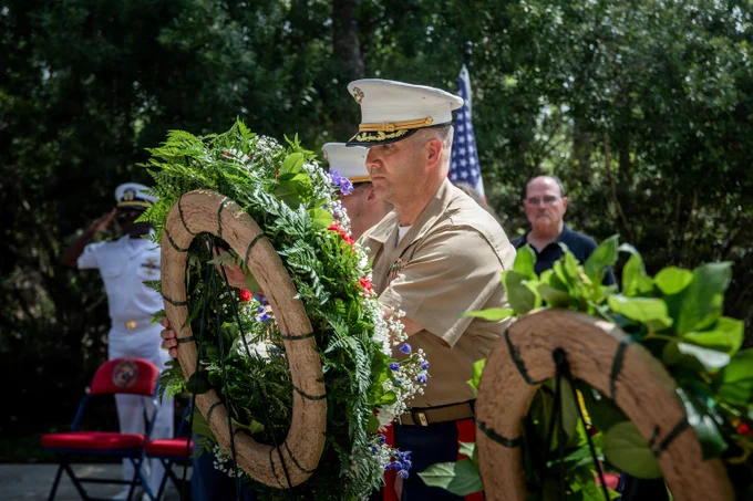 A Marine officer places a ceremonial wreath at a memorial during a wreath-laying ceremony attended by veterans, service members, and family members.