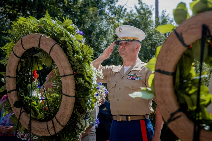 A Marine officer renders a salute beside a memorial wreath during a ceremony honoring fallen military members.