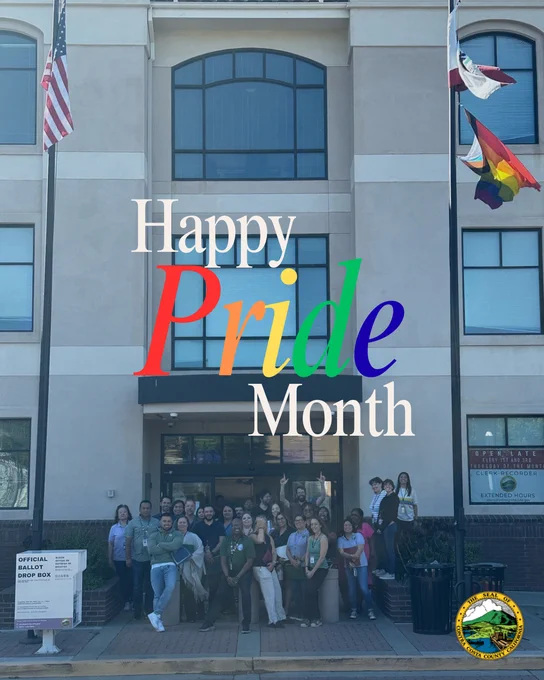 Group of Contra Costa Clerk Recorder Elections Staff gathered in front of the Department building with the American flag, California flag and pride flag, celebrating Pride Month with a colorful 'Happy Pride Month' message overlay.