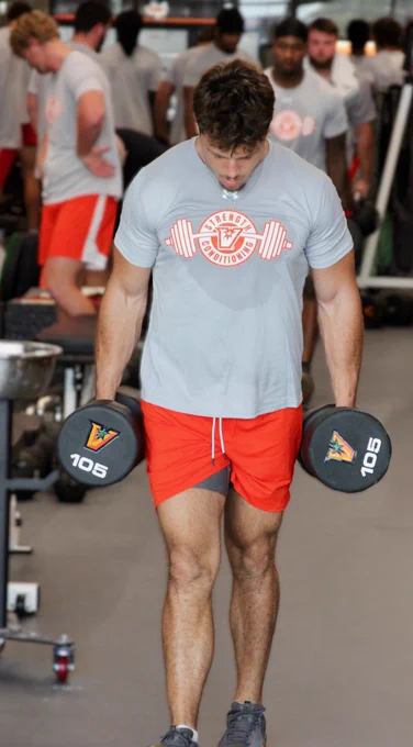 Tyler day in workout attire carrying 105lb dumbbells in each hand