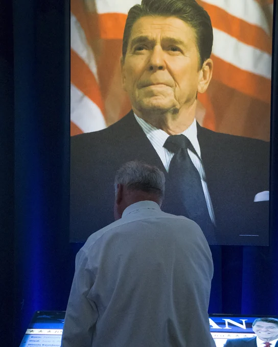 A man stands in front of a large Ronald Reagan photograph in a museum.