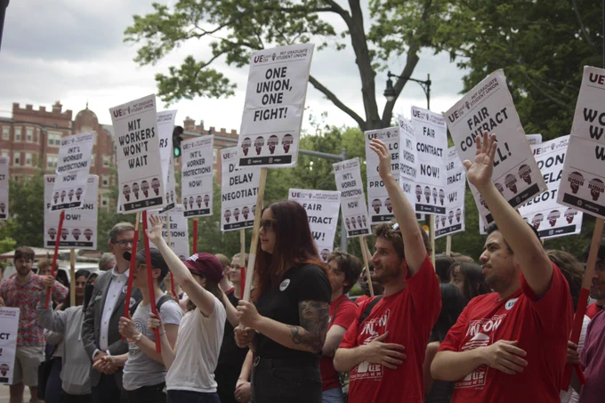 Workers stand together with hands raised
