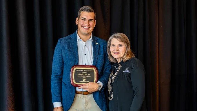 A Purdue Alumni Association representative presents the 2025 Outstanding Young Alumni Award plaque to an alumnus during an awards ceremony.
