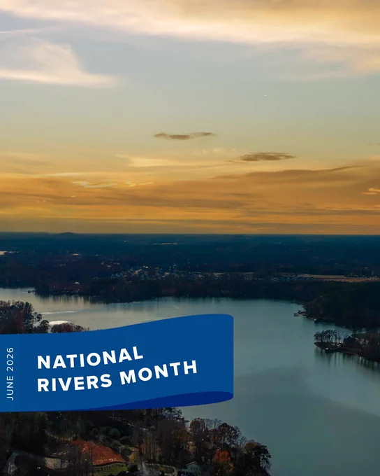 A scenic aerial view of a river surrounded by lush greenery and a distant horizon under a sunset sky. A blue banner on the left reads June 2026 National Rivers Month.