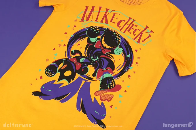 A photo of a yellow shirt with "Mike Check!" written across the top in red in a jagged serif font, above a design showing Cat Mike, Small Mike, and Cowboy Hat Mike appearing to prepare for their ultimate attack. 