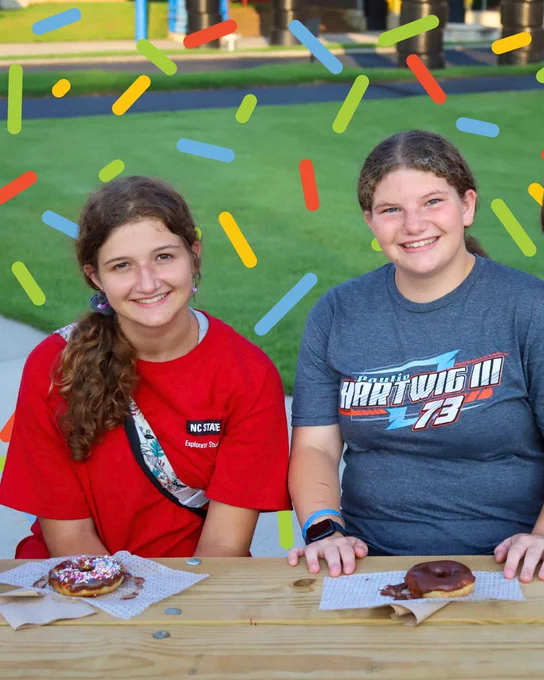 Two Campers at a NASCARnival sitting at a picnic table with their donuts as they smile at the camera.