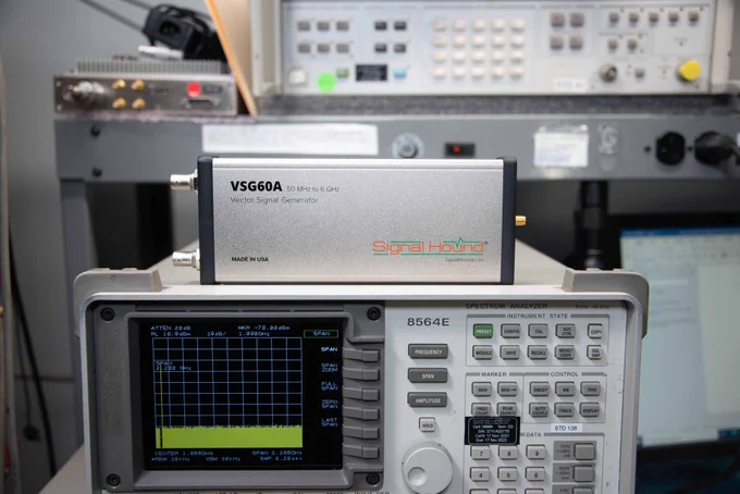 A close-up view of electronic test equipment, including a Signal Hound VSG60A Vector Signal Generator on top and a spectrum analyzer below in a laboratory setting.