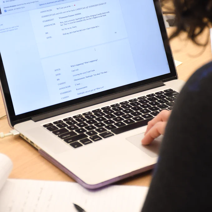 A person is using a laptop with a visible script or text document on the screen. 