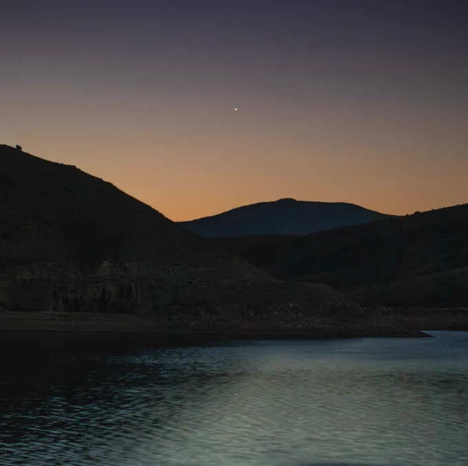 Mars appears as a small, faint, reddish star in a clear pre-dawn sky above a lake rimmed with mountains on June 5, 2026. Photo: NASA/Bill Dunford