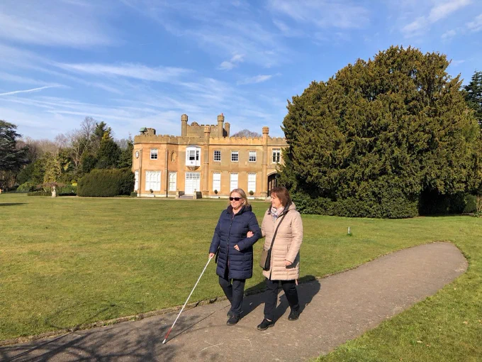 Two women walk arm in arm in from of Nonsuch Mansion on a sunny day