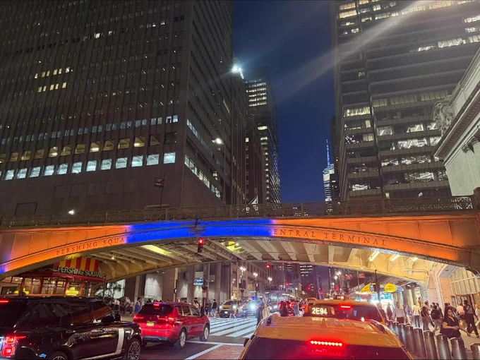Pershing Square Bridge lit in orange and blue lights at Grand Central Terminal in the evening.