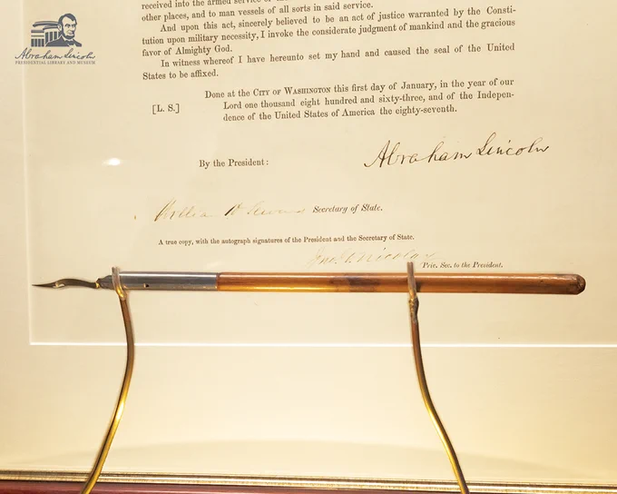 Antique pen displayed on a stand in front of a replica of the Emancipation Proclamation signed by Abraham Lincoln.