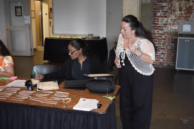 Two women at a registration table with name tags and paperwork in an industrial-style room with exposed brick walls.