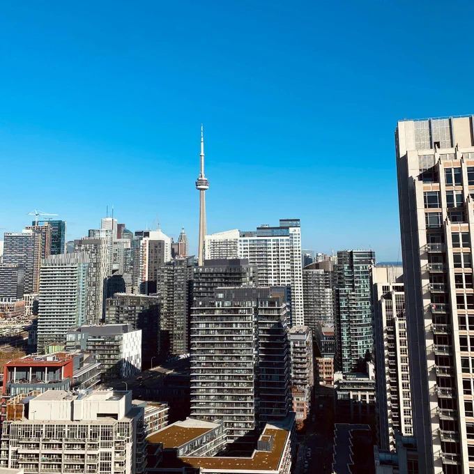 Toronto skyline featuring the CN Tower towering above modern high-rise buildings under a clear blue sky.