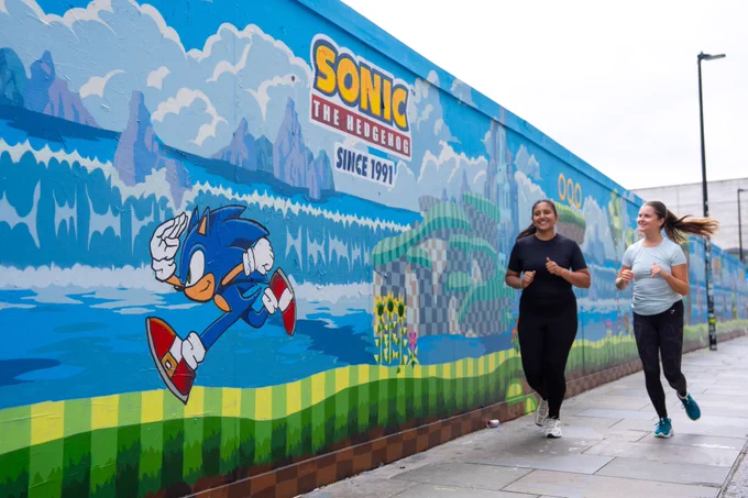 Sonic the Hedgehog mural based on Green Hill Zone. Two women run in front of the mural.
