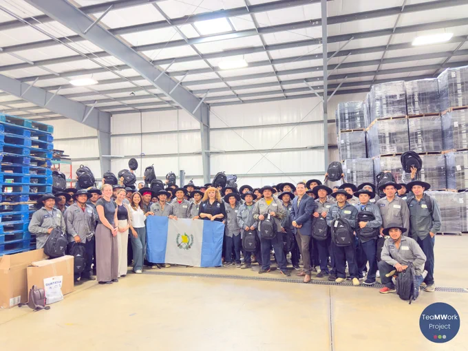 	Los trabajadores se colocan en semicírculo dentro de un almacén para escuchar una presentación del personal del Proyecto TeaMWork sobre los servicios disponibles durante la visita a la granja.
