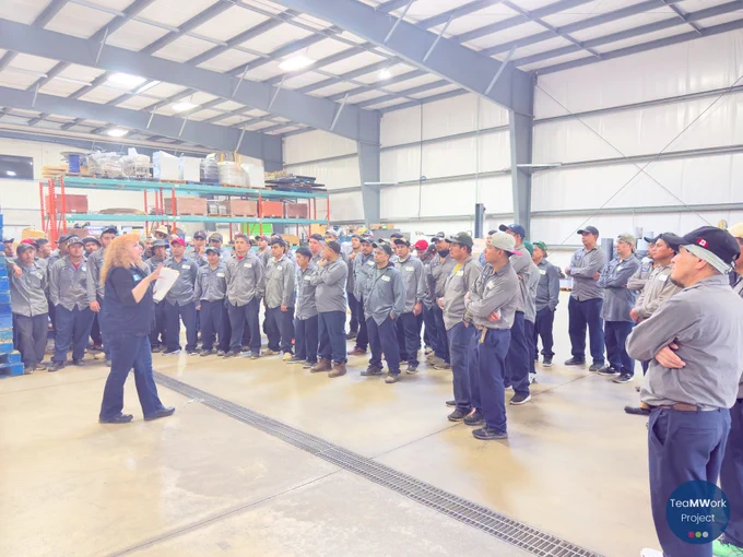Un grupo de trabajadores agrícolas se reunió en el interior de un almacén durante una visita a una granja de Windsor-Essex, mientras escuchaban a un representante del proyecto TeaMWork compartir información y repartir material.
