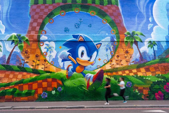 Sonic the Hedgehog mural based on Green Hill Zone. Two women run in front of the mural.