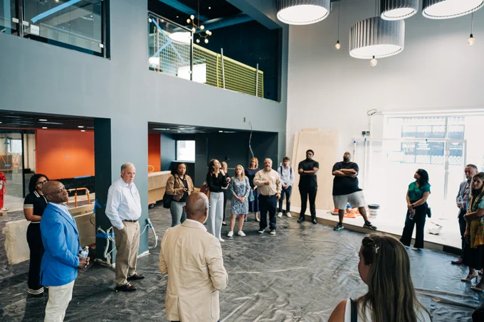 Partners stand in the commons area of the building, which will house the Do Greater Sparkhouse Uptown. The floor is covered and there are elements of construction present. 