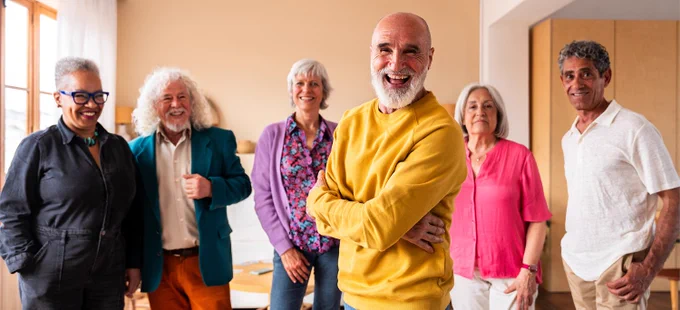 Group of six diverse older adults standing together in a warmly lit 50  center, dressed in casual and attire.