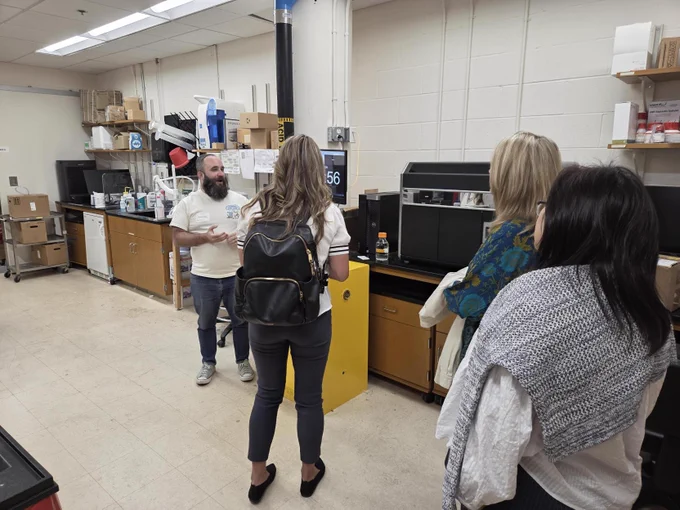 SEASR workshop attendees stand in a core lab as a staff member explains equipment; benches, instruments, and storage shelves line the room.