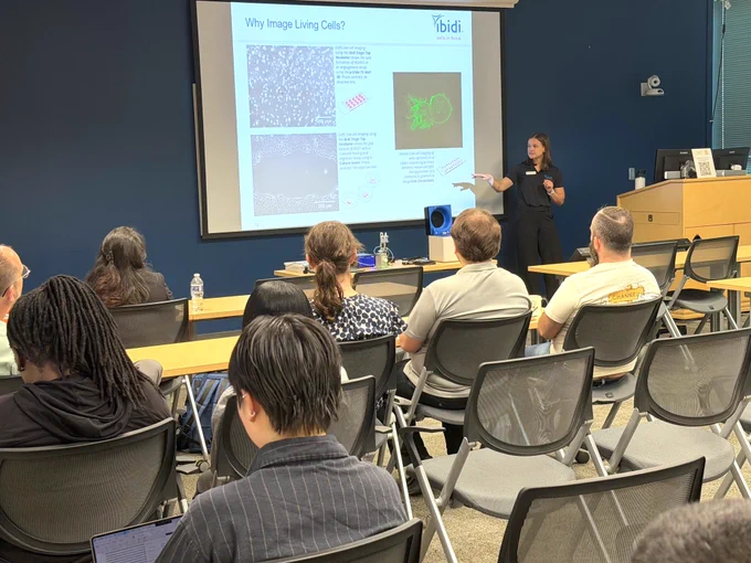 SEASR workshop presenter speaks at the front of a seminar room, pointing to slides on imaging living cells while attendees sit facing the screen.