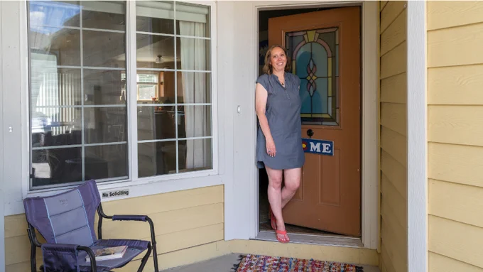 CHFA homeowner Lynn smiling and standing at her front door. 
