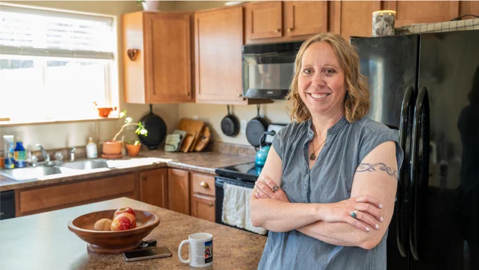 CHFA homeowner Lynn standing cross armed and smiling in her kitchen.