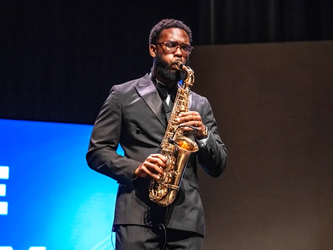 A person is playing a saxophone on stage at the Orange County State of the County event, dressed in formal attire.