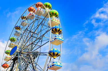 Colorful Ferris wheel cabins with balloon designs against a bright blue sky with scattered clouds.