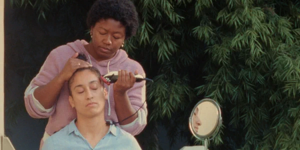 A still from "Hold Me Close" with one person shaving another's head.