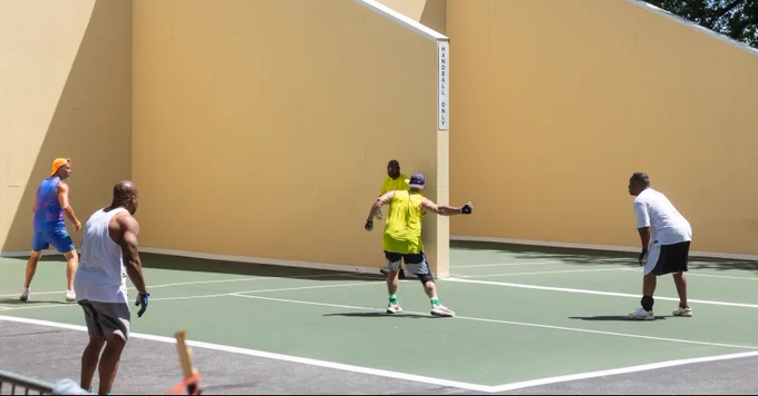 A person wearing a bright yellow shirt is centered among other players at the handball courts in Forest Park. 