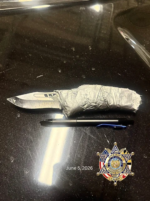 Large knife with a blade marked 'ARMY' and a handle wrapped in duct tape, placed next to a black pen on a dark surface.