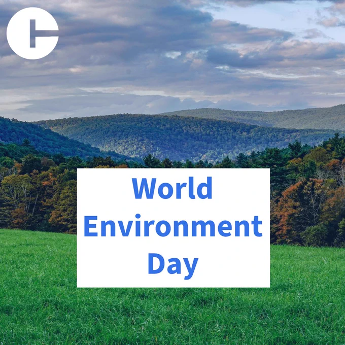 Alt Text: “Scenic landscape with a grassy field in the foreground, forested hills in the middle distance, and a cloudy sky above. A white box centered on the image displays the text ‘World Environment Day.’ A circular white logo with a simple geometric symbol appears in the top-left corner.”