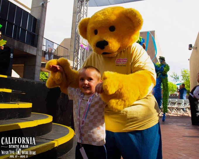 Child holding hands with Poppy the bear during Poppy's Birthday at the California State Fair.