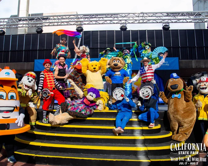 Group of colorful mascots and performers posing on stairs with vibrant costumes and playful expressions during Poppy's Birthday at the California State Fair.