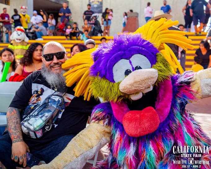 Colorful mascot with purple fur and yellow hair posing with a man during Poppy's Birthday at the California State Fair.