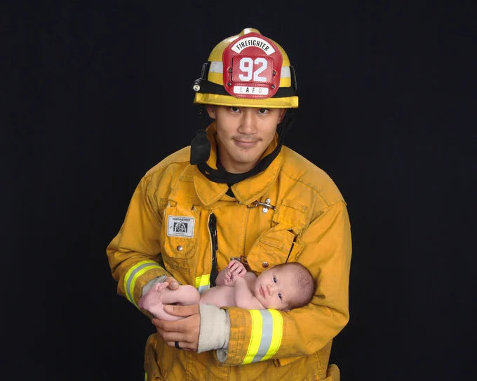 Kelly Wong wearing his firefighting turnouts and holding his child.