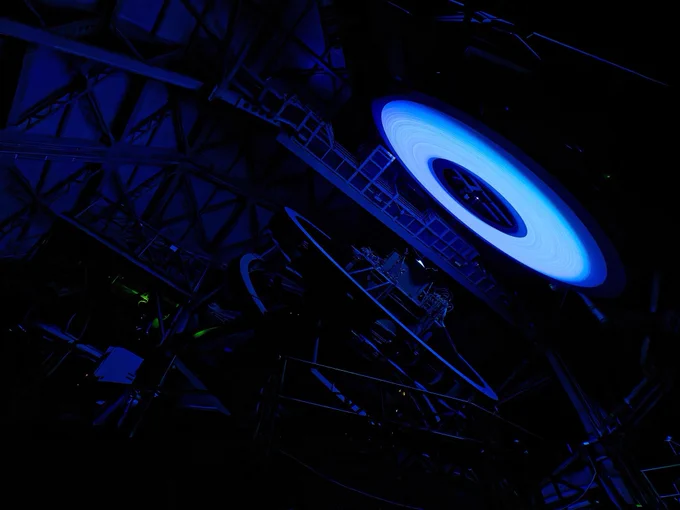 An ominous blue donut-shaped ring glows ominously in the dark to the right. To the left, Rubin's large steel telescope mount structure is barely visible, softly illuminated by the blue glow.