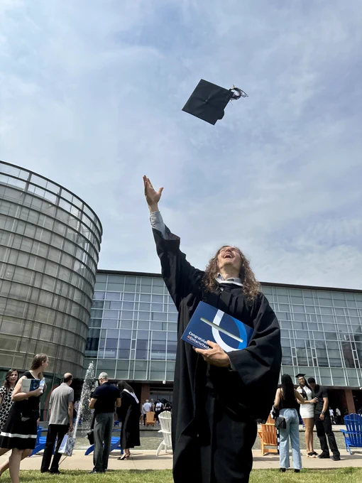 A photo of a graduating student tossing their cap in the air in Polonsky Commons.
