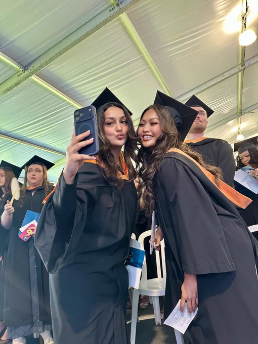 A photo of two graduating students taking a selfie inside the ceremony tent.
