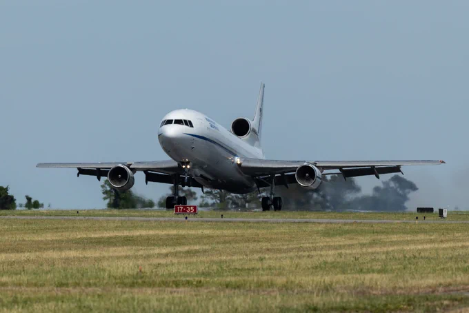 The L-1011 Stargazer aircraft lands on the Wallops runway. The aircraft is white with a blue strip down the side. Photo Credit: NASA/Kyle Hoppes