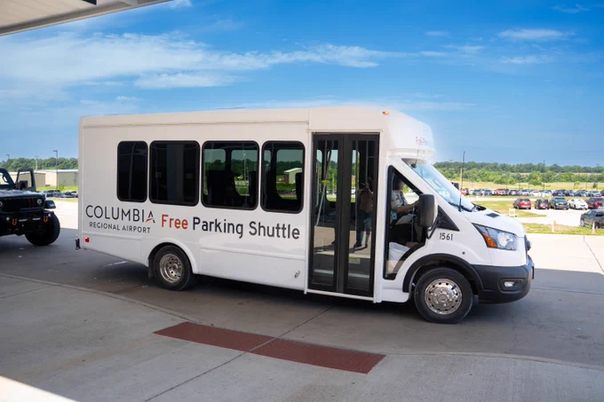 White shuttle bus parked under a canopy at Columbia Regional Airport offering free parking transport service.