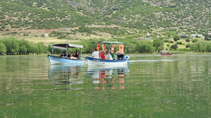 Tourists enjoy a peaceful boat cruise on a scenic lake surrounded by lush hills.
